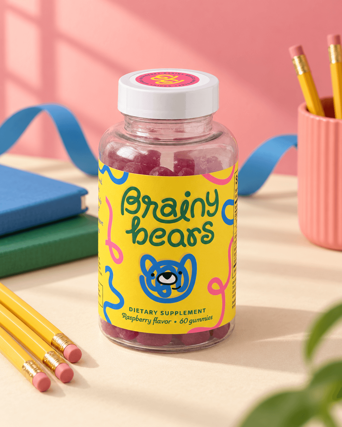 Brainy Bears raspberry gummies beside books and pencils against a coral backdrop.